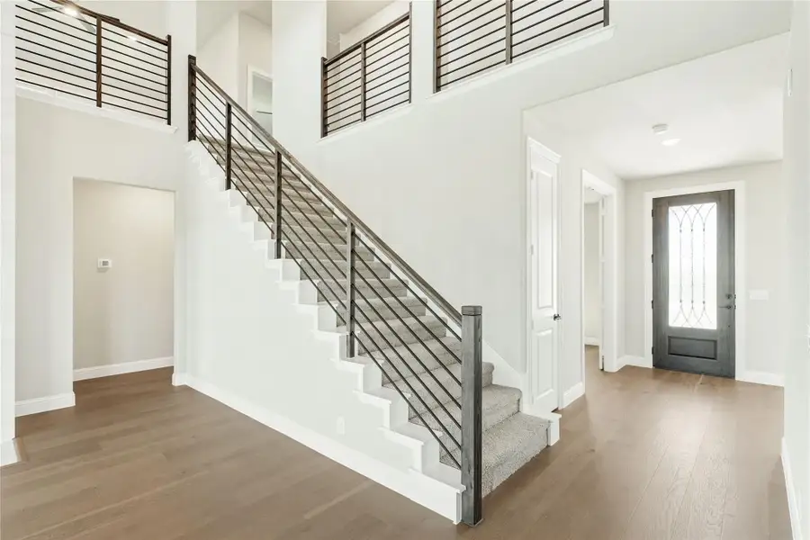 Two-story entryway with carpeted staircase, metal railing, hardwood floors, and glass-panel front door Two-story entryway with carpeted staircase, metal railing, hardwood floors, and glass-panel front door