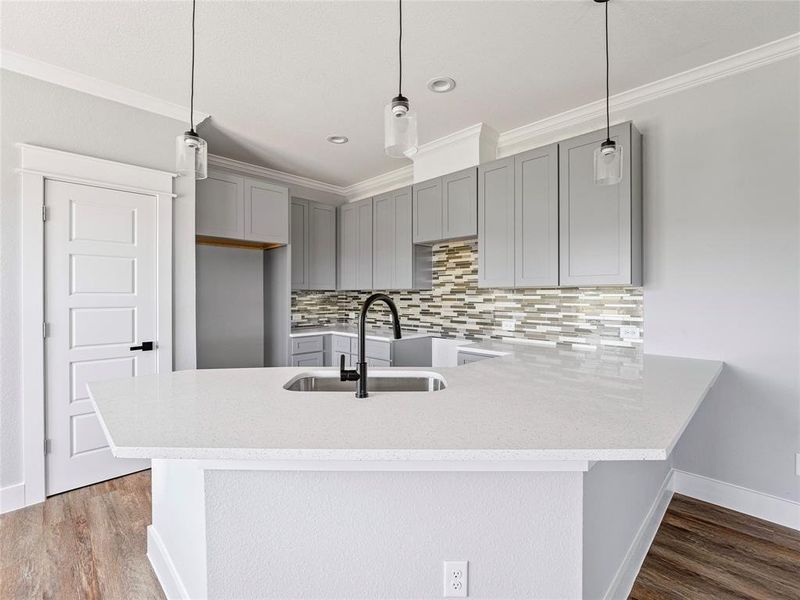 Kitchen with gray cabinetry, a sink, ornamental molding, backsplash, and a peninsula