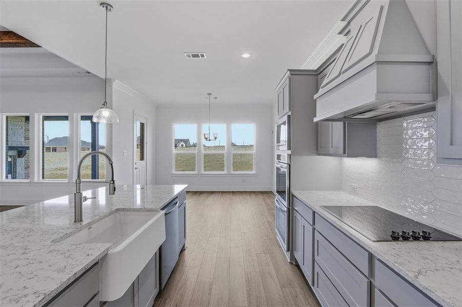 Kitchen with gray cabinets, light stone countertops, pendant lighting, light wood-type flooring, and stainless steel appliances