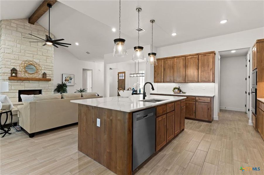 Kitchen featuring brown cabinetry, decorative light fixtures, appliances with stainless steel finishes, a kitchen island with sink, and a fireplace