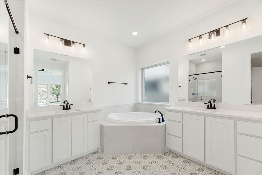 Master bathroom with dual vanities, corner soaking tub, patterned tile floors, and glass shower enclosure
