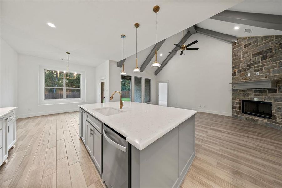 Kitchen featuring hanging light fixtures, gray cabinets, a stone fireplace, light wood finished floors, and high vaulted ceiling