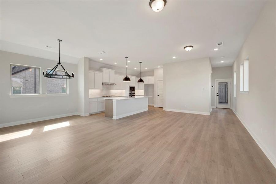 Unfurnished living room featuring light wood-style flooring and suspended lighting