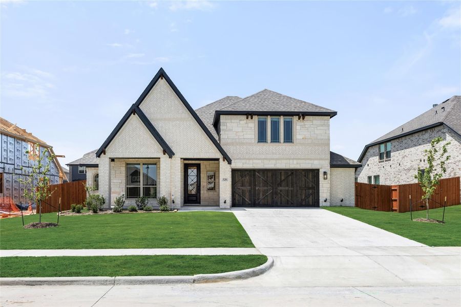 Two-story home with cream brick exterior, steep gabled roofline, and two-car garage with wood doors