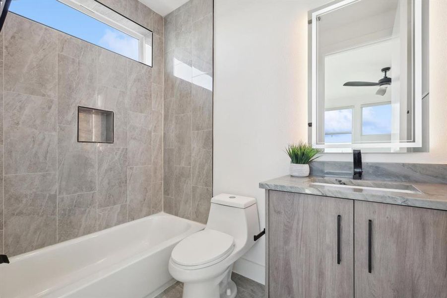 Full bathroom featuring vanity, ceiling fan, tiled shower / bath combo, toilet, and tile patterned flooring