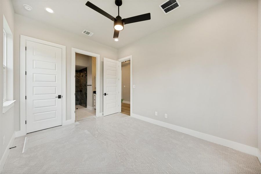A quiet secondary primary bedroom on the main level with light carpet offers easy access to the attached bathroom through a modern paneled door. A quiet secondary primary bedroom on the main level with light carpet offers easy access to the attached bathroom through a modern paneled door.