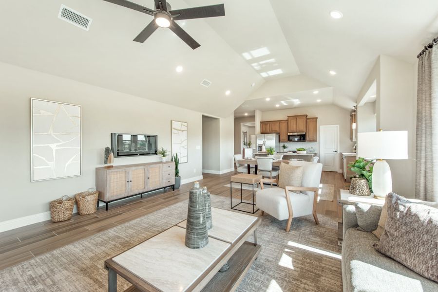 Open-concept living room with vaulted ceiling, ceiling fan, and wood-look floors, open to dining area and kitchen beyond.