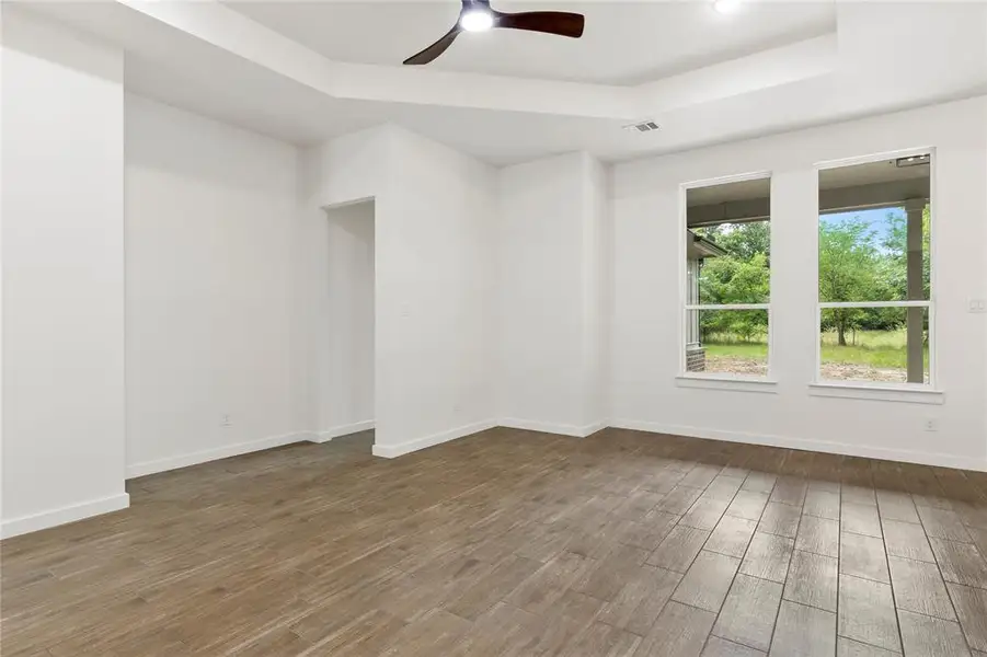 Spacious room featuring wood-finish flooring, a tray ceiling, and a ceiling fan