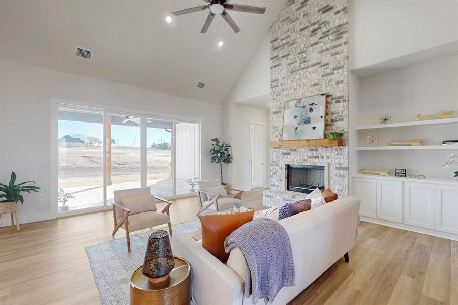 Living room featuring a large fireplace, built in features, high vaulted ceiling, and light hardwood / wood-style floors