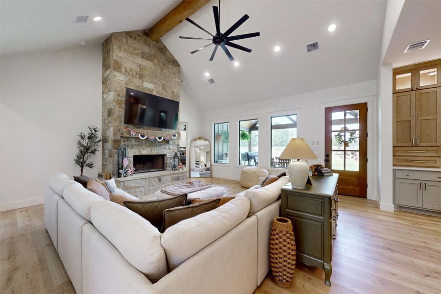 Living area with high vaulted ceiling, beamed ceiling, a ceiling fan, a fireplace, and light wood-style floors