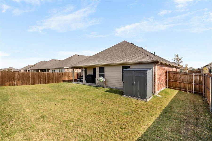 Rear view of house featuring a shingled roof, a fenced backyard, brick siding, a patio area, and an outbuilding