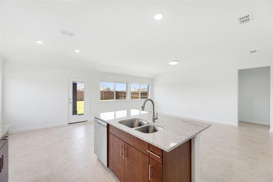 Kitchen island with granite countertop, double sink, and dark wood cabinets in open-concept layout with tile floors