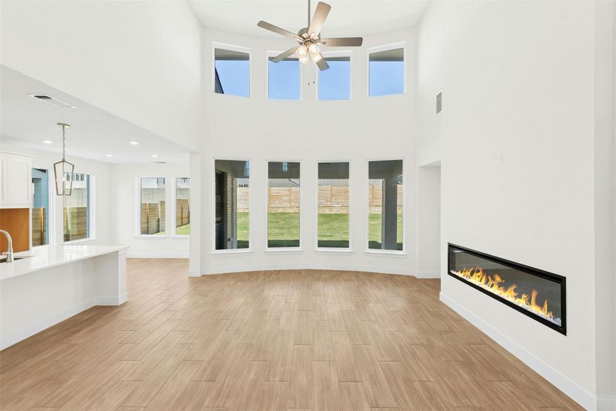 Unfurnished living room with a glass covered fireplace, light wood-style floors, plenty of natural light, a high ceiling, and recessed lighting