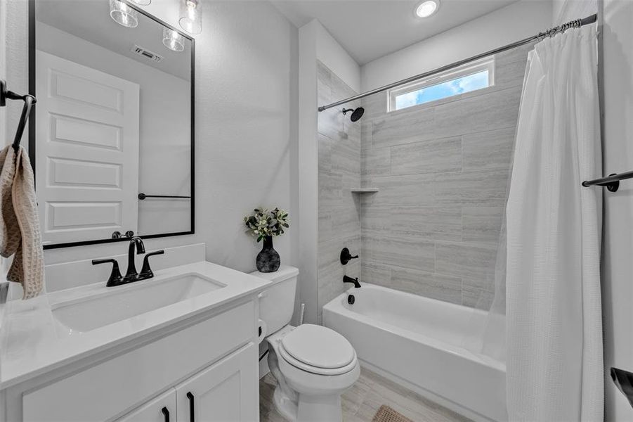 Full bathroom featuring a white vanity with integrated sink, black plumbing fixtures, and a shower-tub combination with light-toned tiled walls
