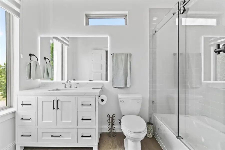 Contemporary bathroom featuring a spacious white vanity with matte black hardware, a rectangular illuminated mirror, and a glass-enclosed shower-tub combination