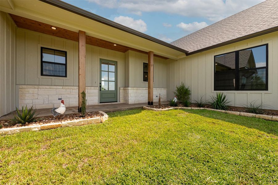 Property entrance featuring covered porch, a yard, roof with shingles, and board and batten siding
