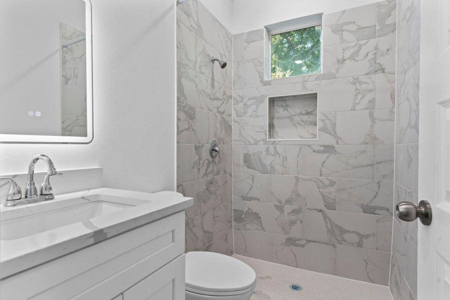 Sleek bathroom with a frameless walk-in shower and LED-lit mirror.