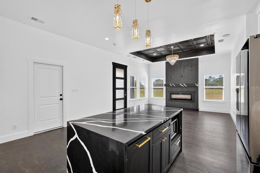 Central kitchen island featuring a black countertop with white veining, gold hardware, and built-in microwave