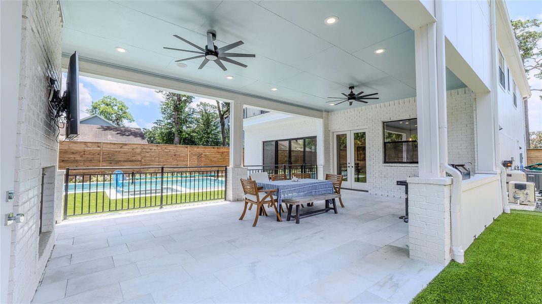 Beautiful covered patio with ceiling fans, outdoor dining area, and a view of a fenced-in pool. Ideal for entertaining and relaxation.