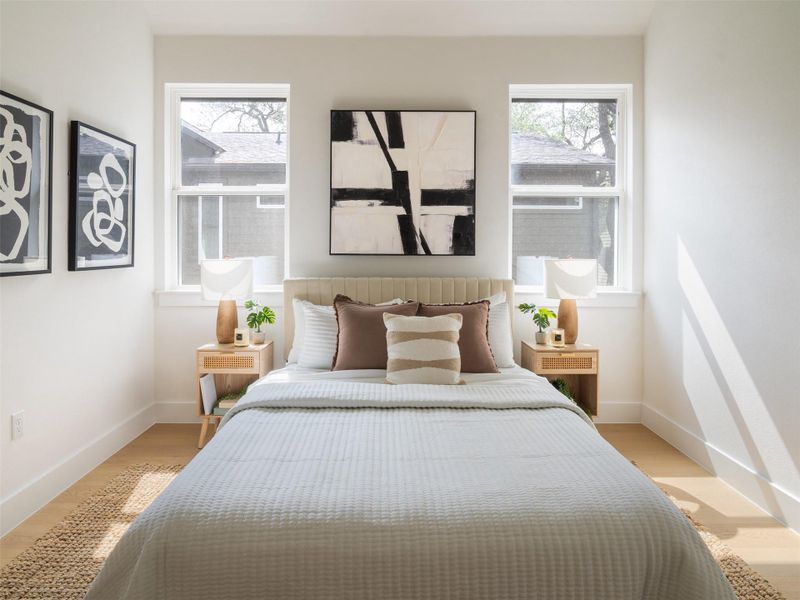 Bedroom featuring wood-finish flooring, two large windows, and a plush upholstered headboard