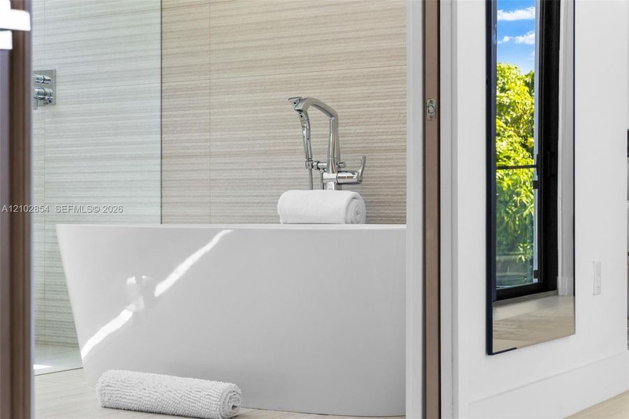 Freestanding soaking tub with a polished chrome floor-mounted faucet and textured tile wall accents