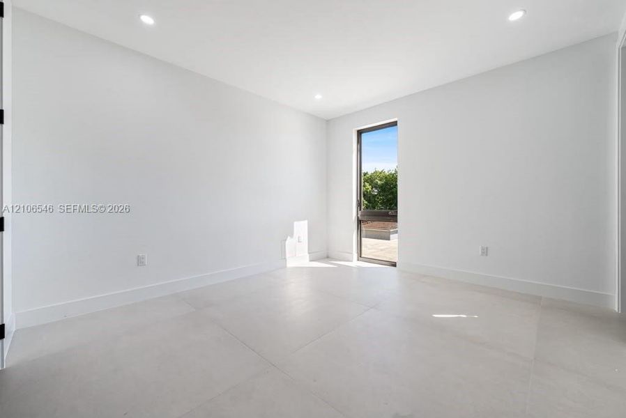 Minimalist room featuring large-format tile flooring, recessed ceiling lighting, and a floor-to-ceiling glass panel door