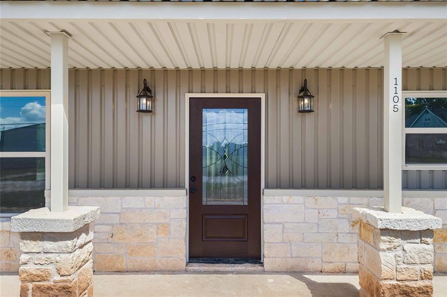 Doorway to property featuring board and batten siding, covered porch, and stone siding