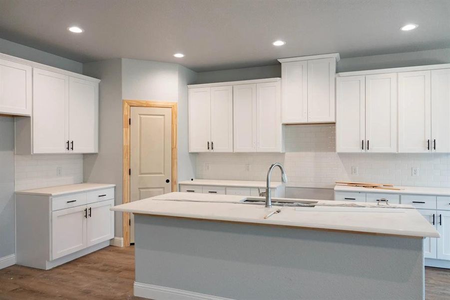 Kitchen with backsplash, wood-type flooring, a center island with sink, and white cabinets