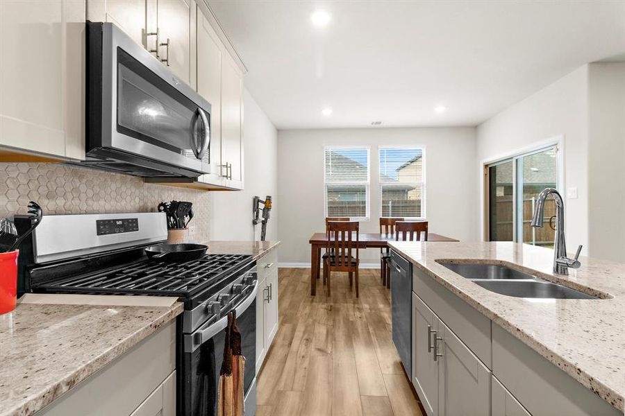Kitchen with stainless steel appliances, decorative backsplash, light wood-type flooring, recessed lighting, and light stone counters Kitchen with stainless steel appliances, decorative backsplash, light wood-type flooring, recessed lighting, and light stone counters