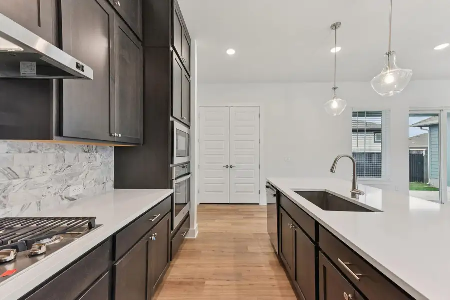Modern kitchen featuring dark wood-finish cabinetry, light stone countertops, and a full tile backsplash