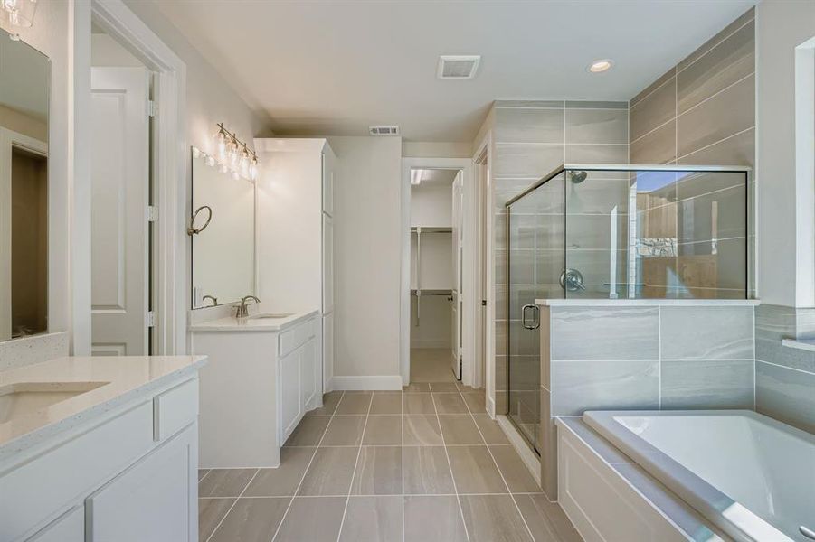 Full bathroom featuring two vanities, a stall shower, a garden tub, light tile patterned floors, and recessed lighting