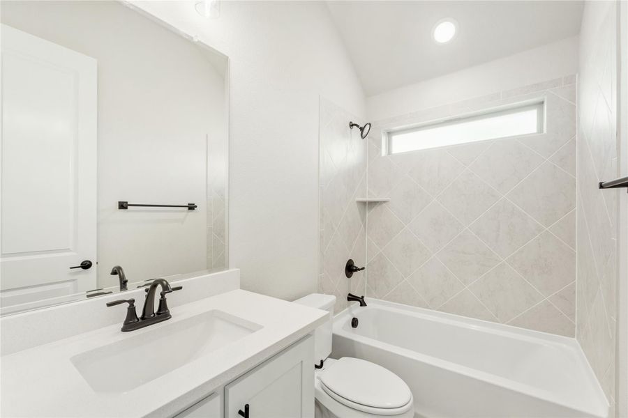 Full bathroom with white vanity, toilet, and tub-shower combo with diagonal tile surround and dark hardware. Full bathroom with white vanity, toilet, and tub-shower combo with diagonal tile surround and dark hardware.