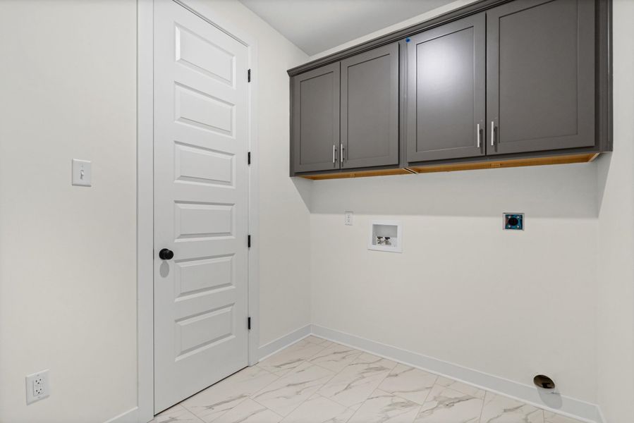 Laundry space featuring light-toned tile flooring, white walls, and built-in gray cabinetry with brushed nickel hardware Laundry space featuring light-toned tile flooring, white walls, and built-in gray cabinetry with brushed nickel hardware