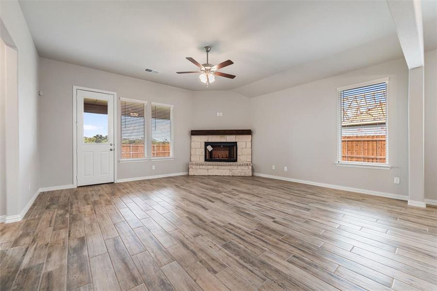 Unfurnished living room featuring a stone fireplace, light wood finished floors, a ceiling fan, and lofted ceiling Unfurnished living room featuring a stone fireplace, light wood finished floors, a ceiling fan, and lofted ceiling