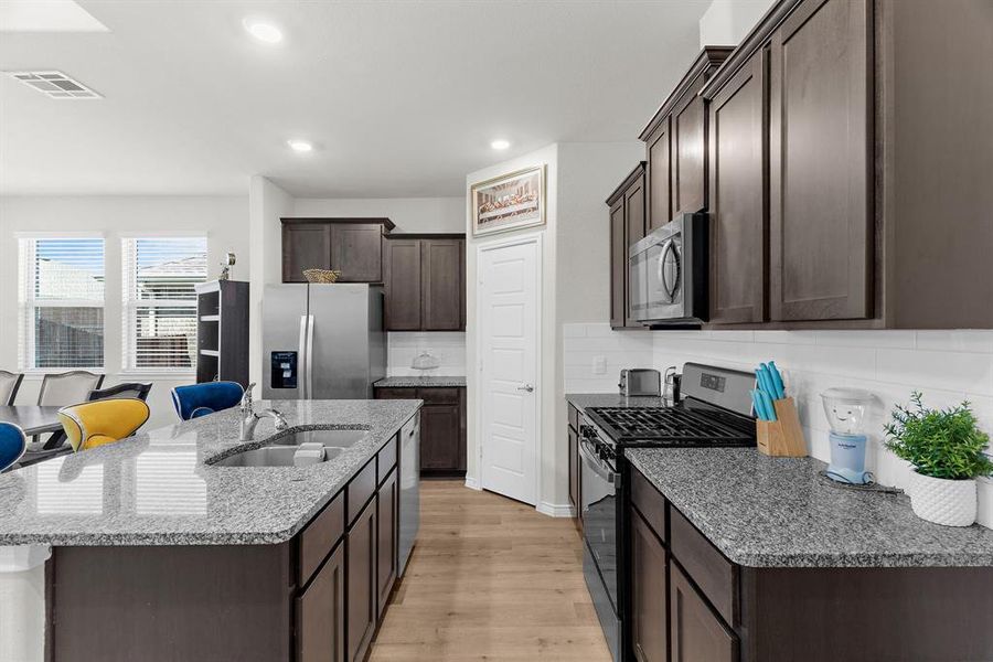 Kitchen with a sink, light wood finished floors, appliances with stainless steel finishes, visible vents, and dark brown cabinets