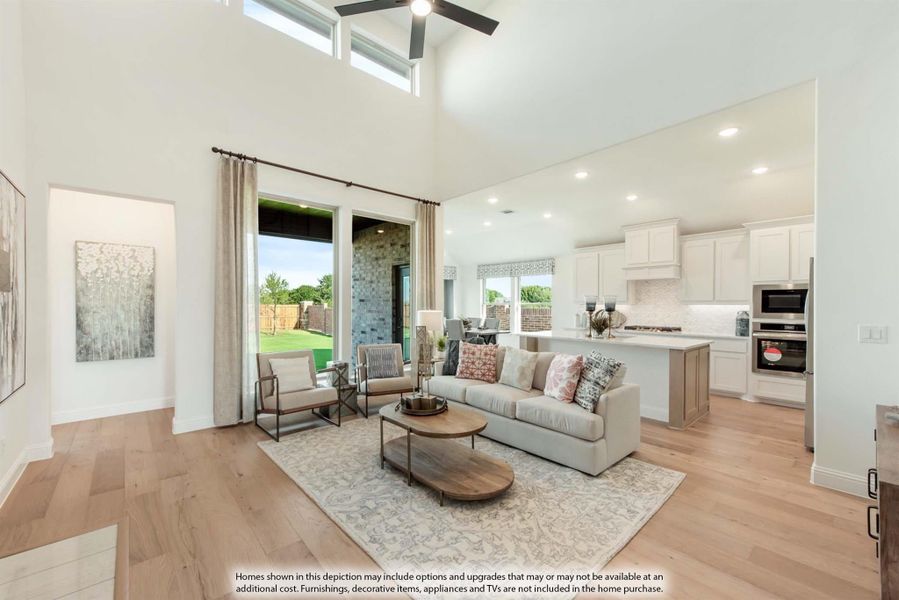 Open-concept living room with two-story ceiling, hardwood floors, and kitchen visible in background
