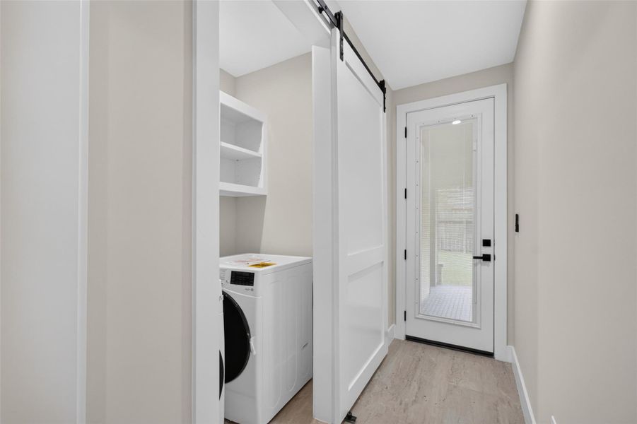 Bright and functional laundry room with modern appliances, sleek shelving, and a convenient sliding barn door, leading to a glass-paneled exterior door for easy outdoor access.