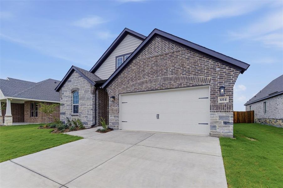 Traditional-style home featuring a brick and stone facade, two-car garage, concrete driveway, and established landscaping
