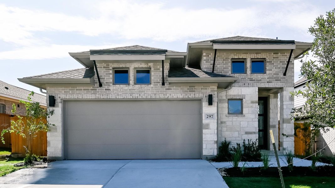 View of front facade featuring driveway, stone siding, and roof with shingles