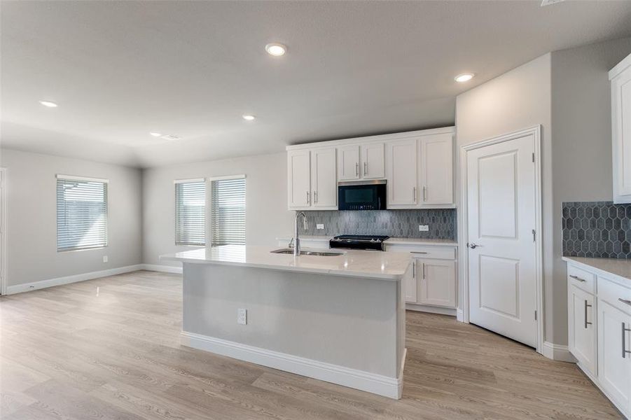 Kitchen with light stone counters, a center island with sink, decorative backsplash, white cabinetry, and recessed lighting