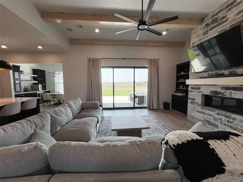 Living room with beam ceiling, recessed lighting, wood finished floors, a stone fireplace, and a ceiling fan