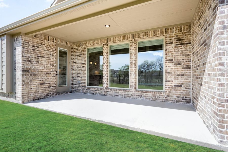 Covered back patio with concrete slab, brick exterior, and large windows overlooking green lawn
