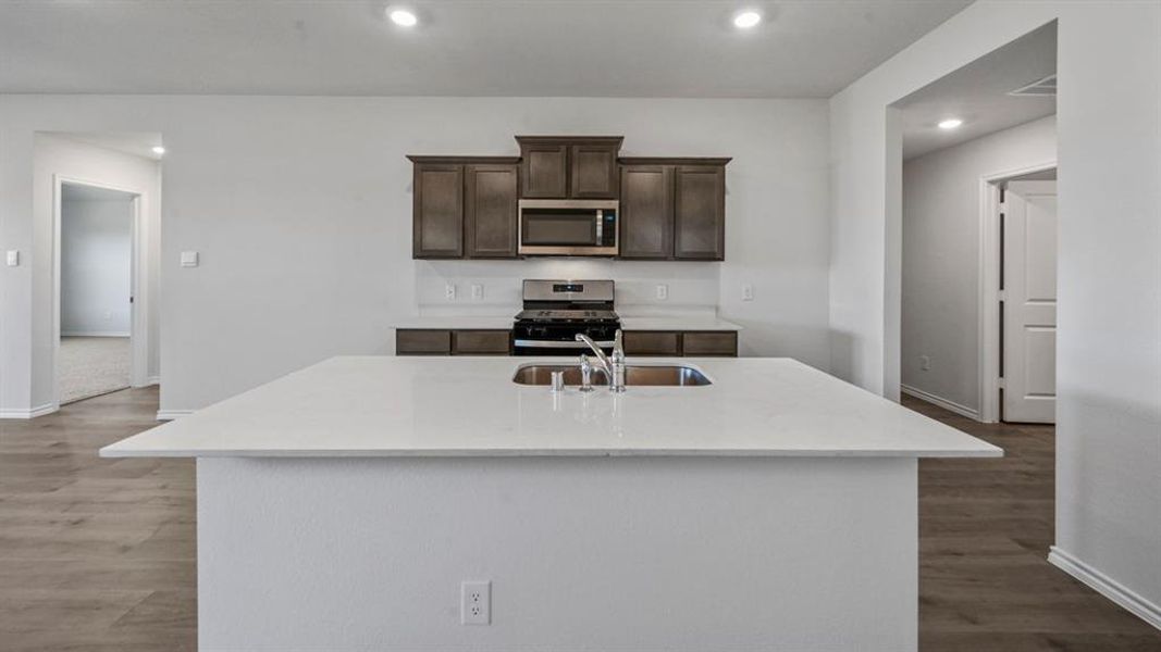 Kitchen showcasing a spacious island with an undermount sink, complemented by white countertops and wood-finish flooring