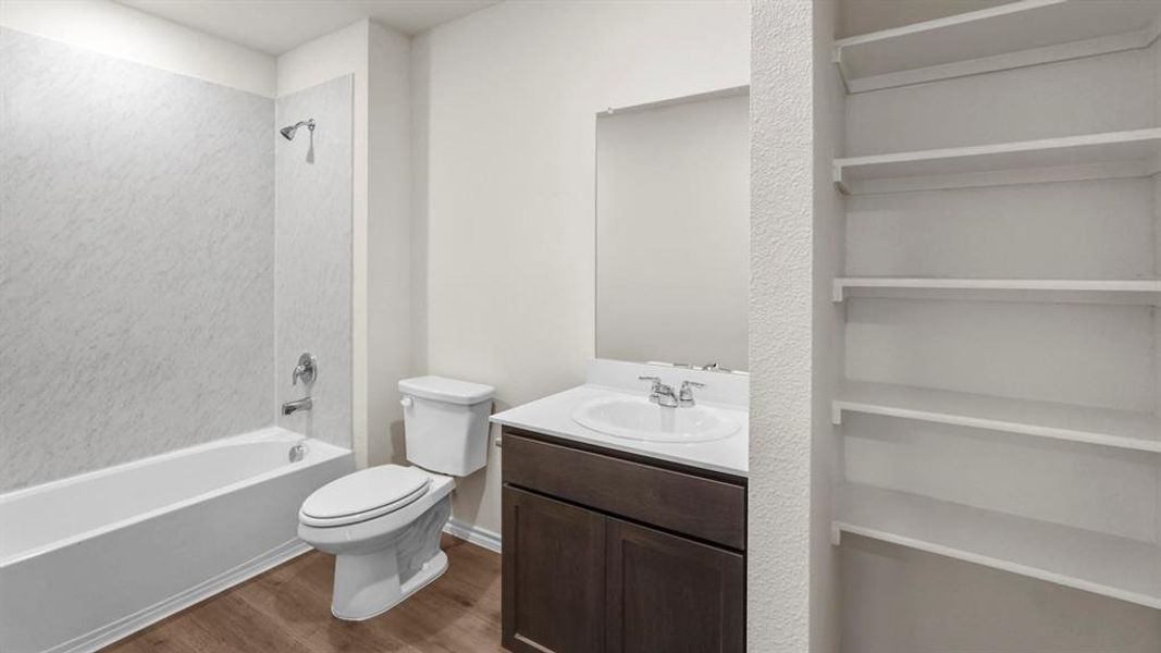 Bathroom featuring a bathtub with a shower, a toilet, a dark wood vanity with a white countertop and sink, and built-in shelving