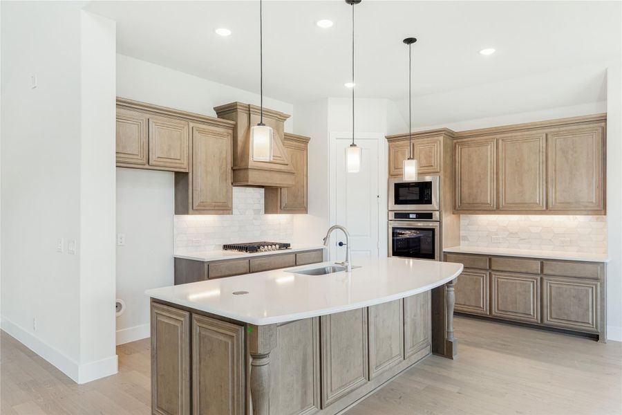 Kitchen with large center island, tan wood cabinets, white countertops, and stainless steel appliances Kitchen with large center island, tan wood cabinets, white countertops, and stainless steel appliances
