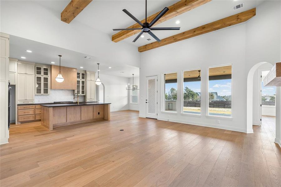 Kitchen featuring open floor plan, a center island with sink, ceiling fan, glass insert cabinets, and light wood-style floors