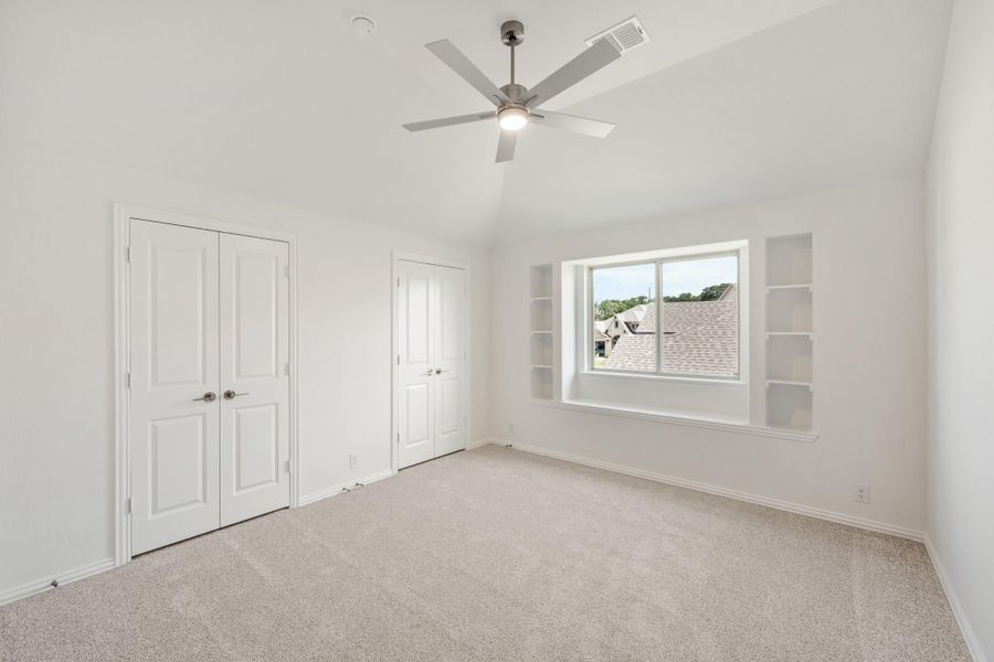Empty bedroom with carpet, ceiling fan, two closets, and built-in shelves beside a window Empty bedroom with carpet, ceiling fan, two closets, and built-in shelves beside a window