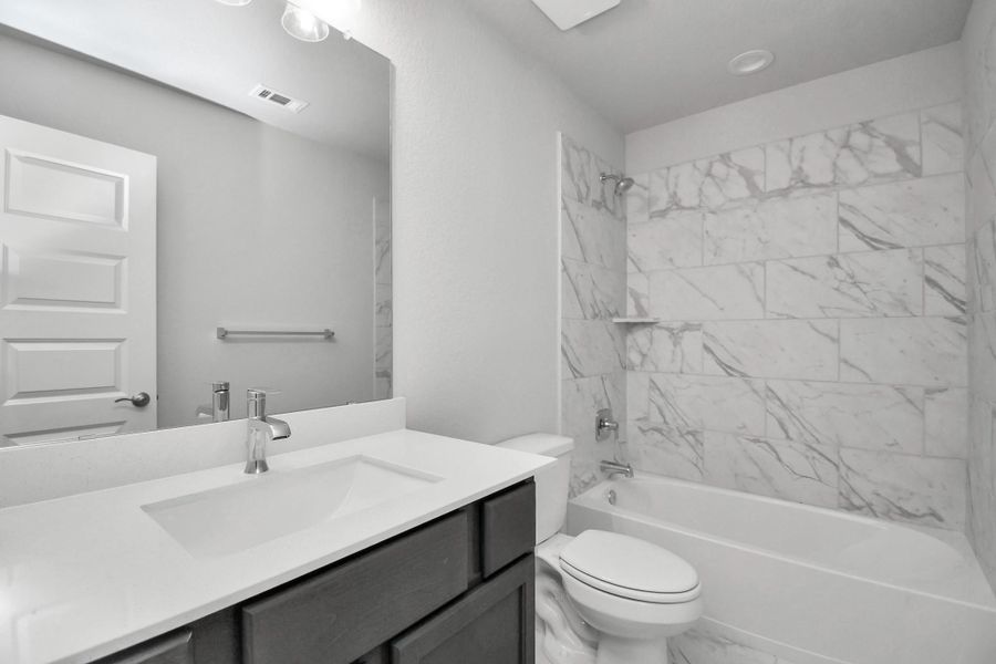 Secondary bath features tile flooring, bath/shower combo with tile surround, light stained wood cabinets, beautiful light countertop. Sample photo of completed home with similar floor plan. Actual colors and selections may vary. Secondary bath features tile flooring, bath/shower combo with tile surround, light stained wood cabinets, beautiful light countertop. Sample photo of completed home with similar floor plan. Actual colors and selections may vary.