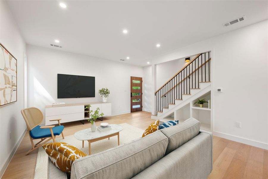 A well-lit living space features light wood flooring, an open staircase with modern railings, and clean white walls. A well-lit living space features light wood flooring, an open staircase with modern railings, and clean white walls.