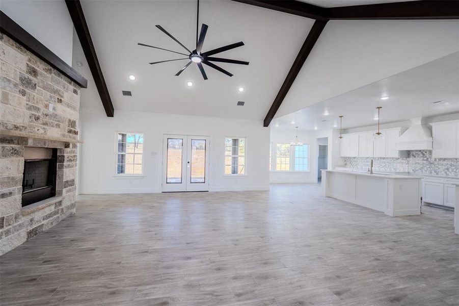 Unfurnished living room with beamed ceiling, a stone fireplace, light wood-style flooring, high vaulted ceiling, and a chandelier Unfurnished living room with beamed ceiling, a stone fireplace, light wood-style flooring, high vaulted ceiling, and a chandelier
